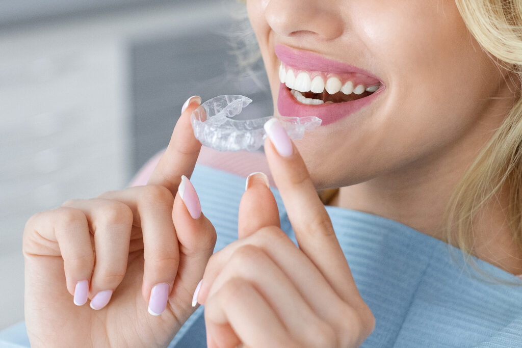 smiling woman holding clear aligners in front of mouth