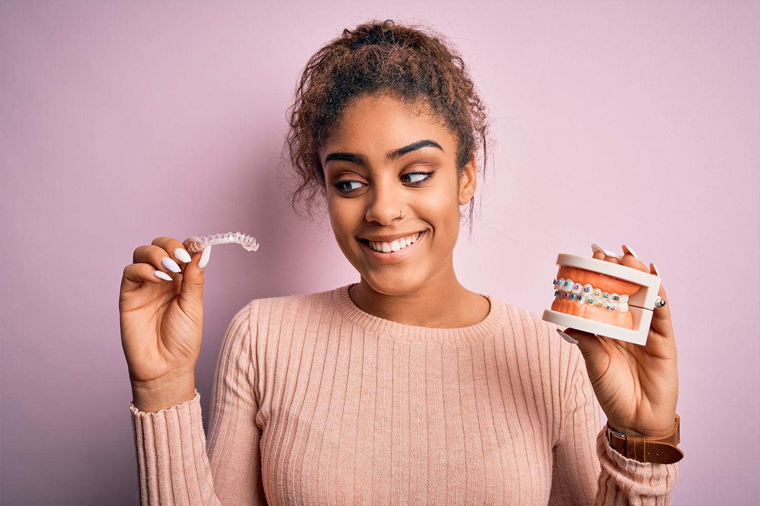 smiling woman holding clear aligners and teeth model with braces