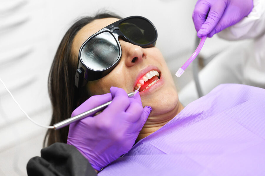 gloved hands performing laser teeth cleaning on patient wearing eye protection