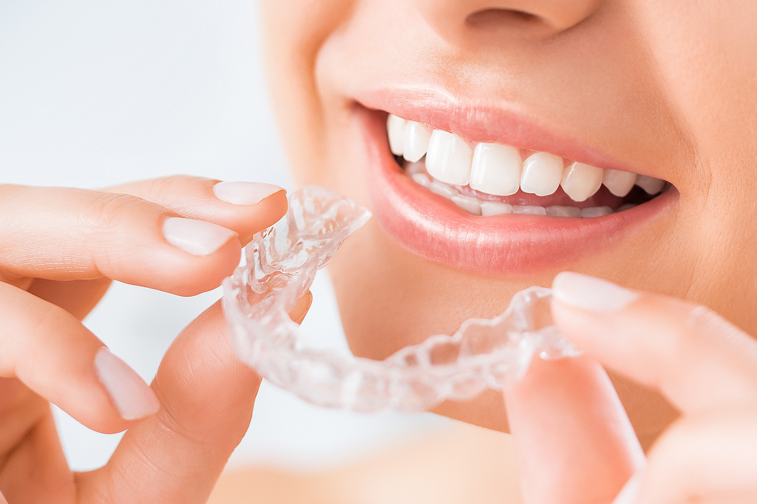 smiling woman holding clear aligners in front of her mouth