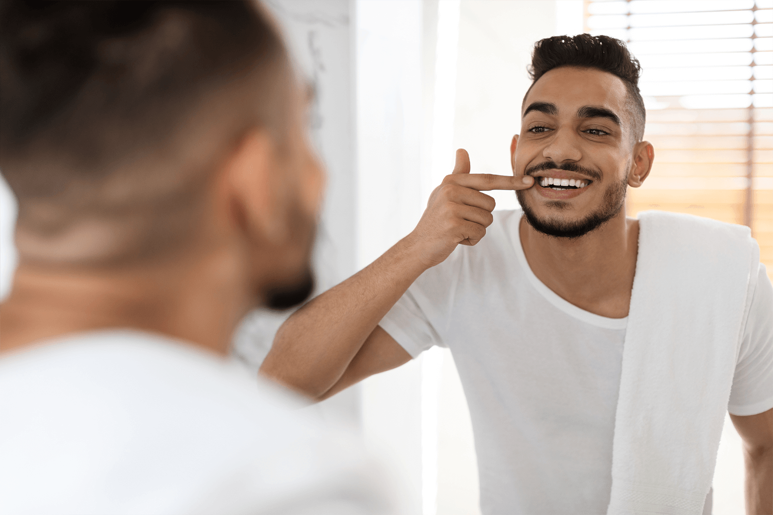 man smiling into mirror and pointing at teeth