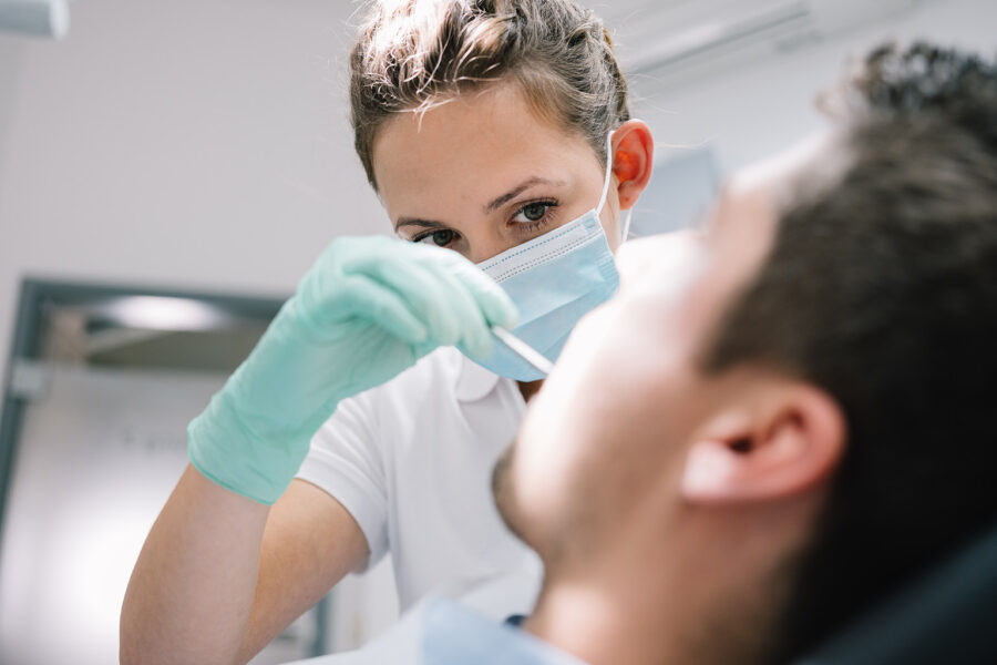 female dentist using dental tool in male patient's mouth