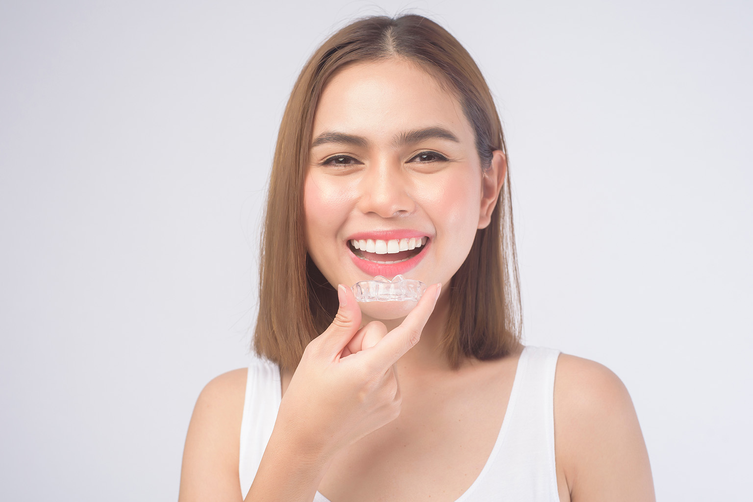 smiling woman holding clear aligner in front of mouth