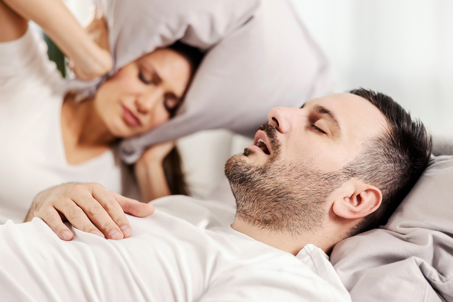 man asleep on his back while woman covers her ears with pillow