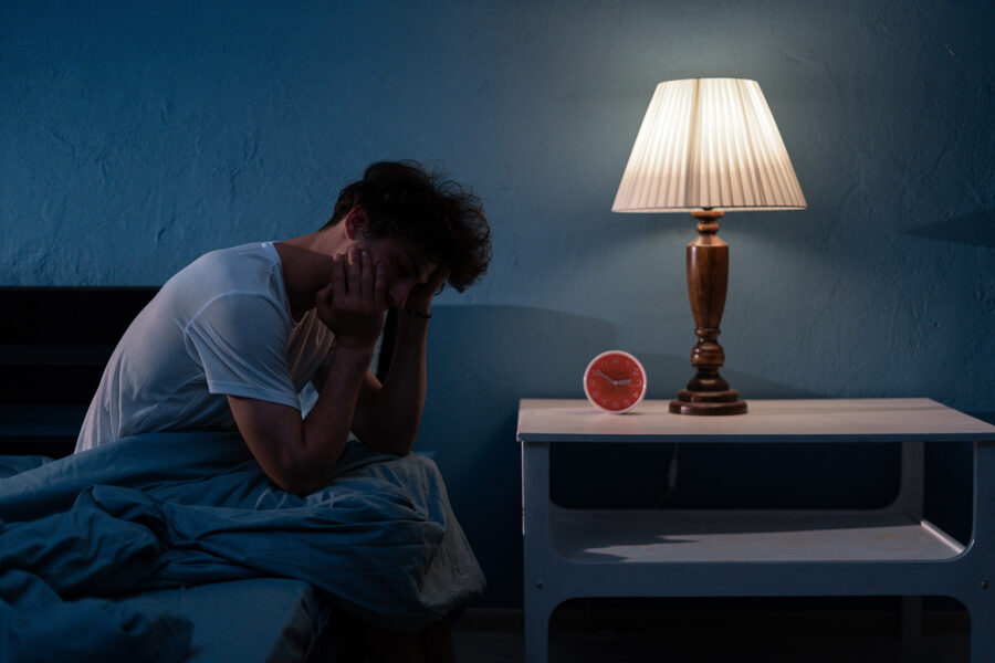 man sitting on side of bed holding head in hands