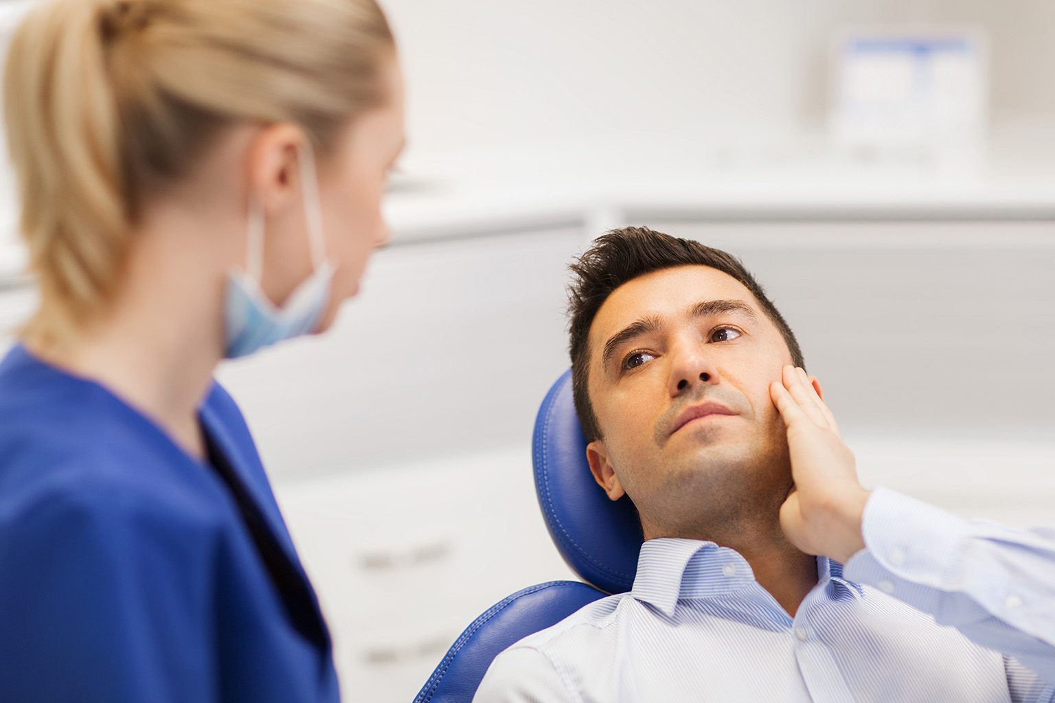 man holding his jaw in pain looking at dentist