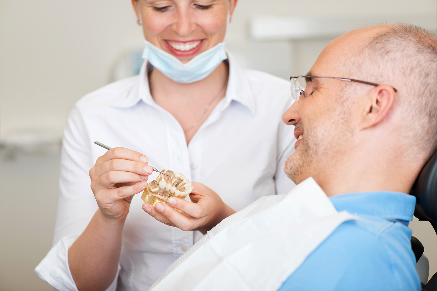 dentist holding a mouth model with implants in front of patient