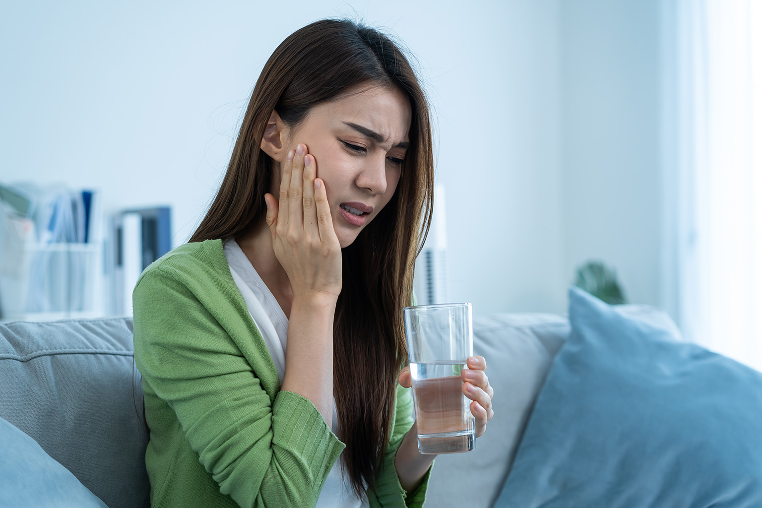 woman holding her jaw in pain holding a glass of water