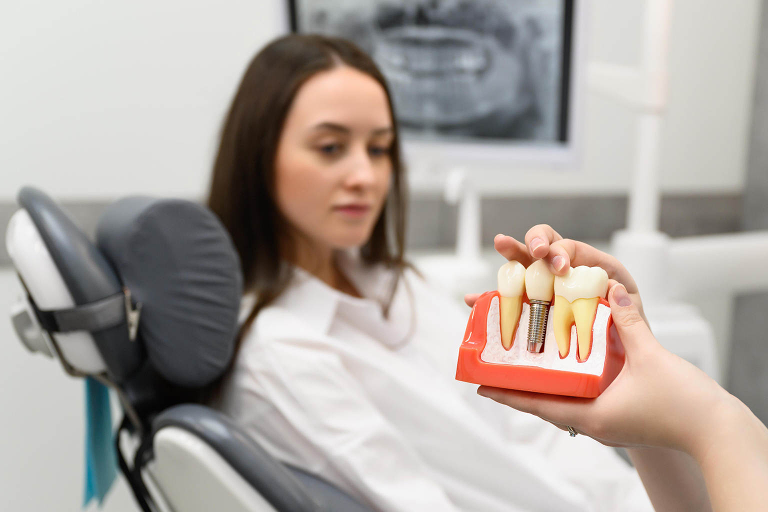 hands holding mouth model with implant in front of woman