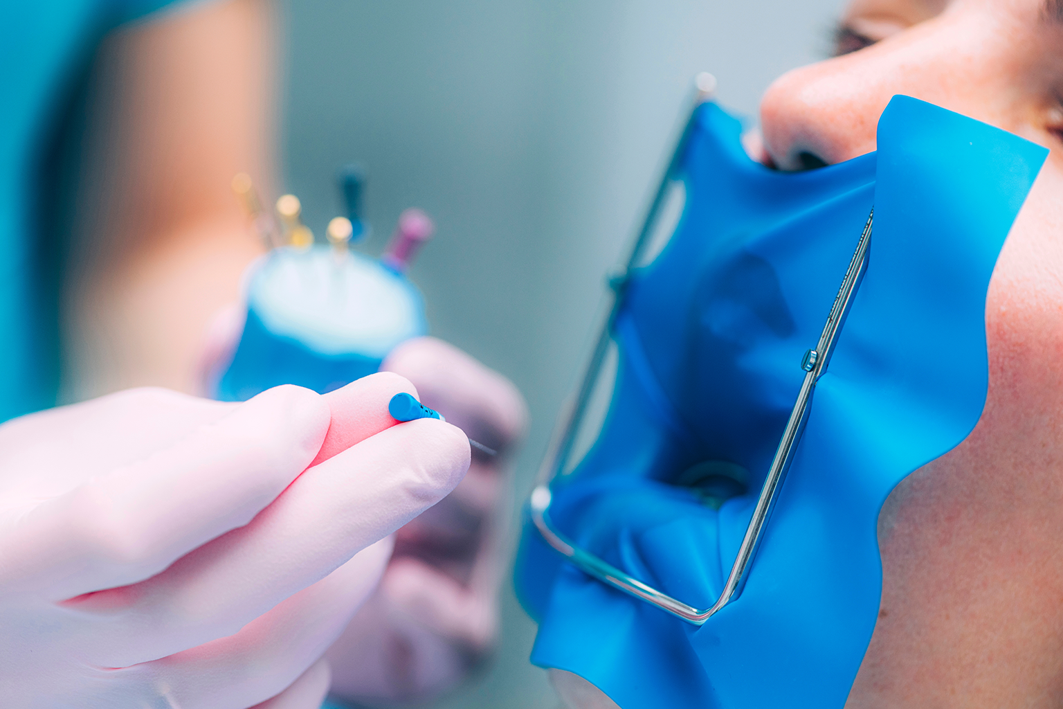 gloved hands holding dental tools in front of patient's mouth