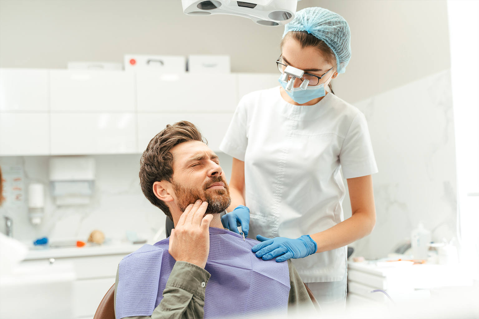 dentist looking down at man holding jaw in pain