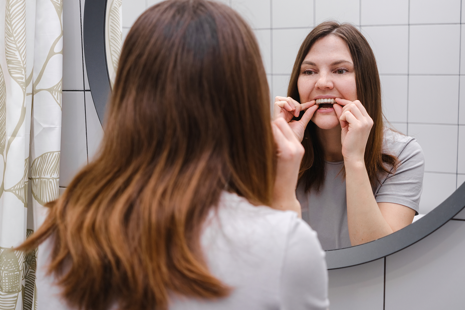 woman placing clear aligner in her mouth looking in mirror