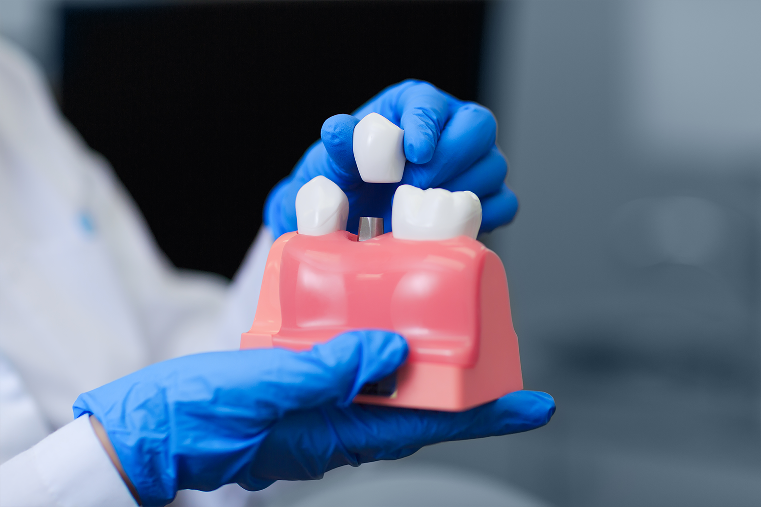 gloved hands placing dental crown on gum model