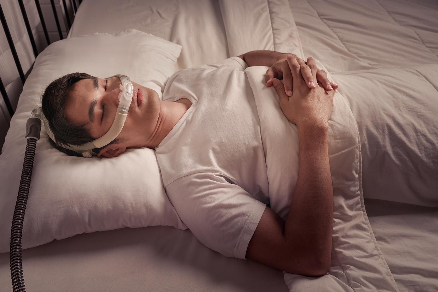 man asleep on his back in bed wearing a cpap mask