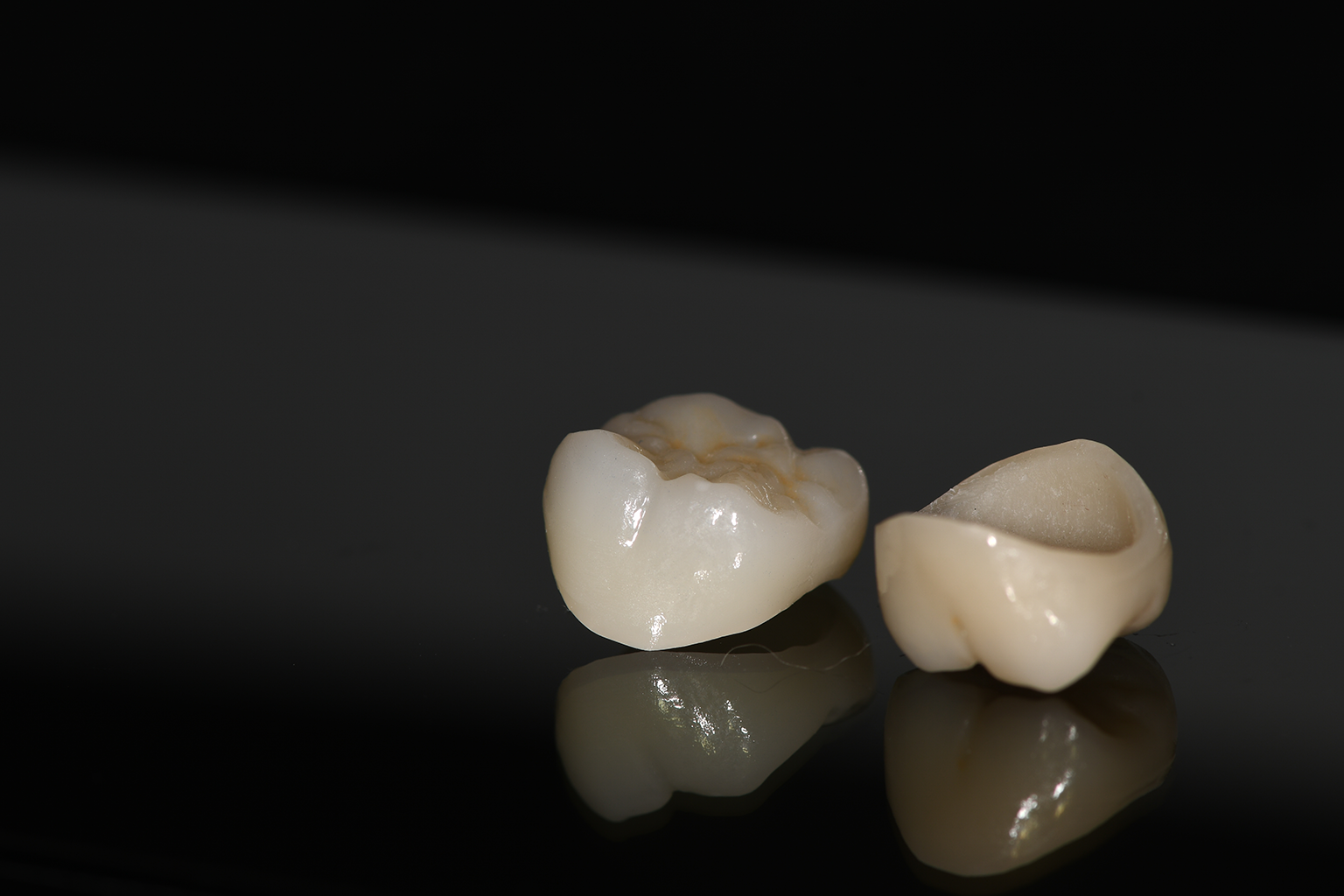 two dental crowns on dark surface