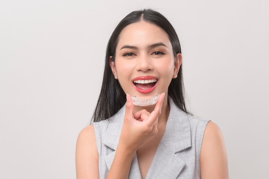 woman holding clear aligner in front of her smile