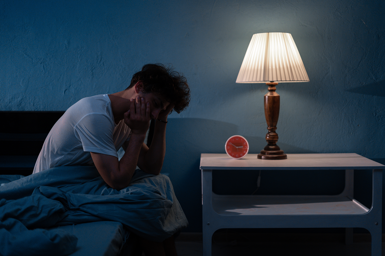 man sitting on side of bed holding his head