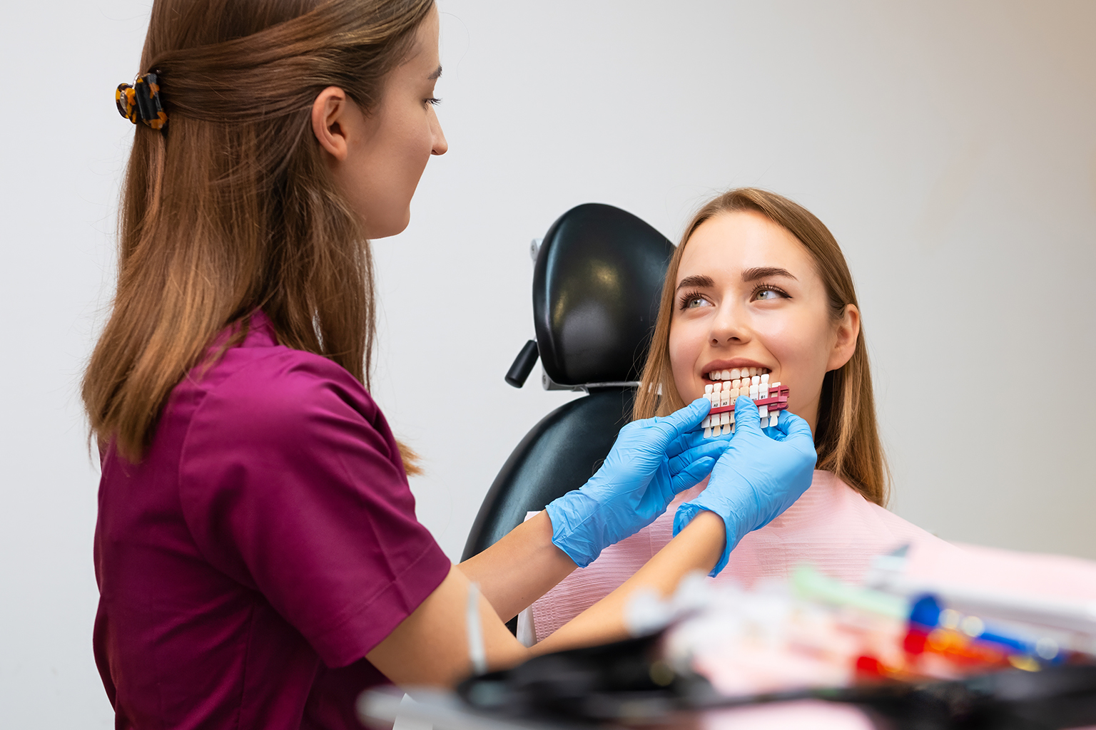 dentist holding shade-matching tool against woman's smile