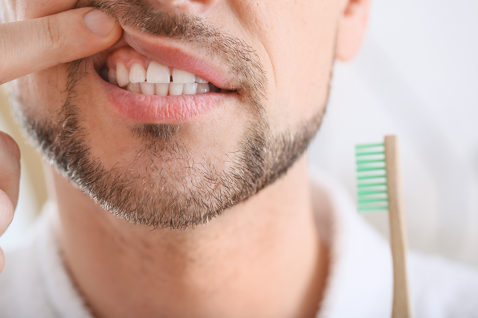 man holding tooth brush lifting lip to show gums