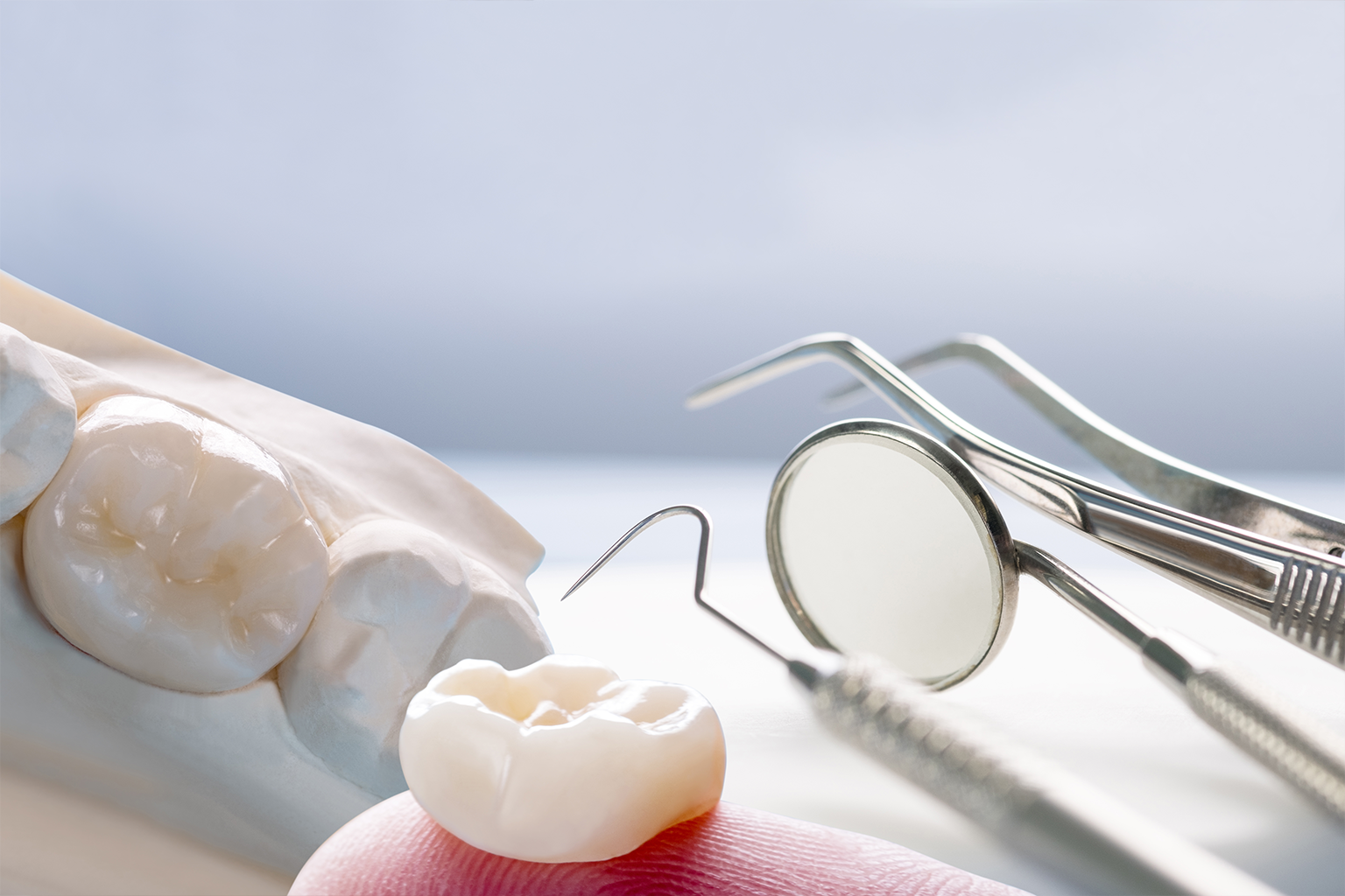 dental crown on finger tip in front of model jaw and dental tools