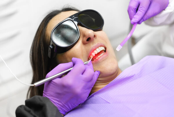 gloved hands using dental laser in patient's mouth