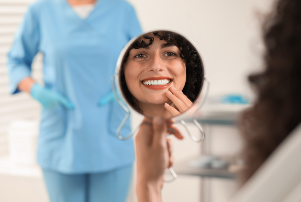woman smiling into hand mirror in dental office
