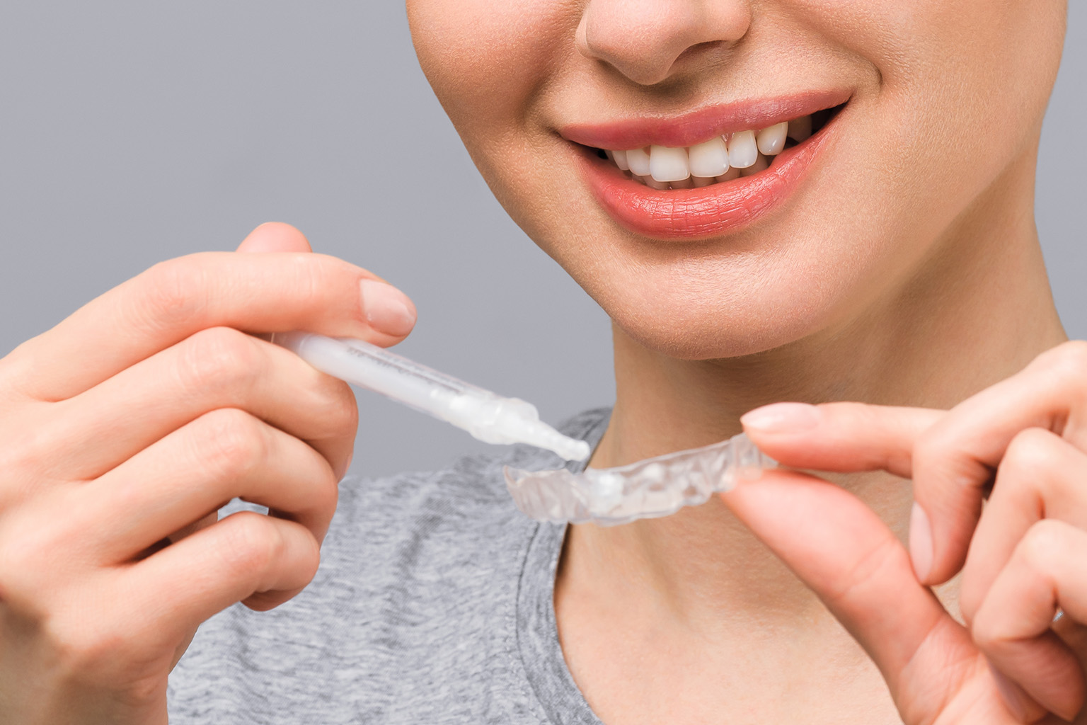 smiling woman squirting whitening gel into whitening tray