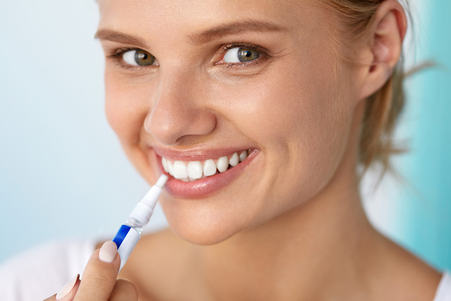 smiling woman applying whitening gel onto her teeth