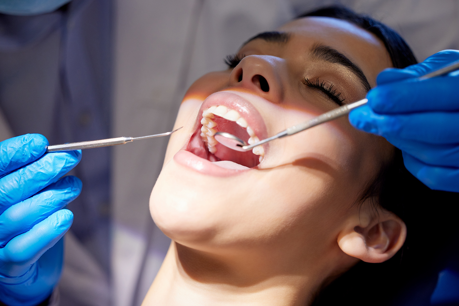 gloved hands holding dental tools in woman's mouth