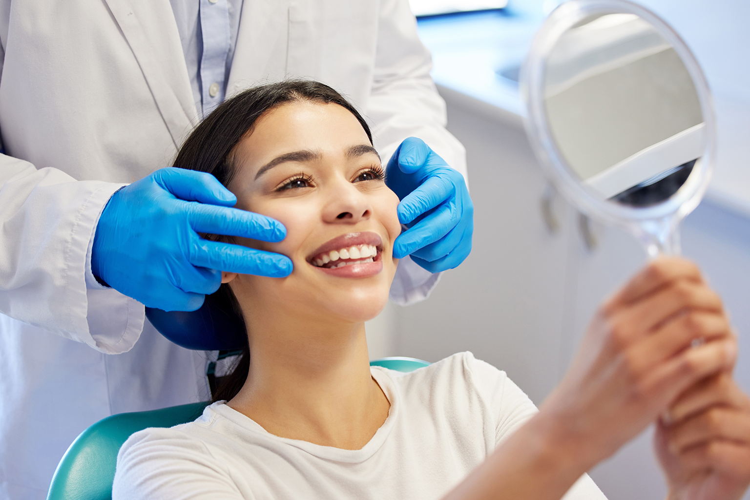 gloved hands framing smile of woman looking into handheld mirror