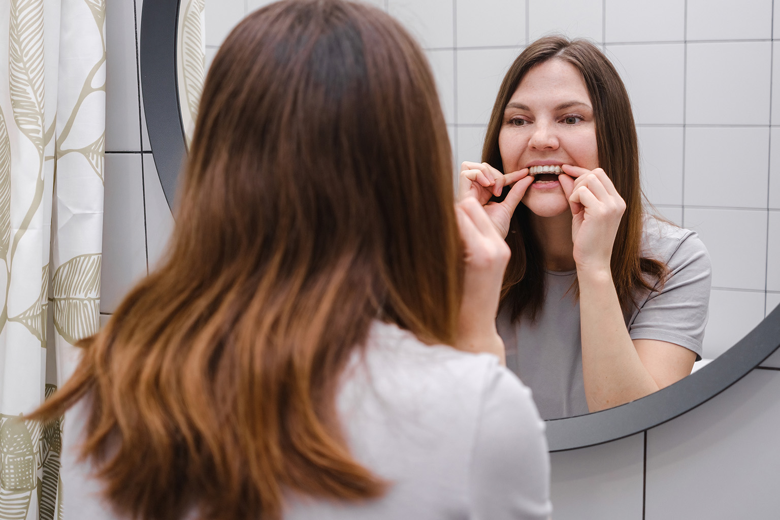woman looking in mirror while placing clear aligner in mouth