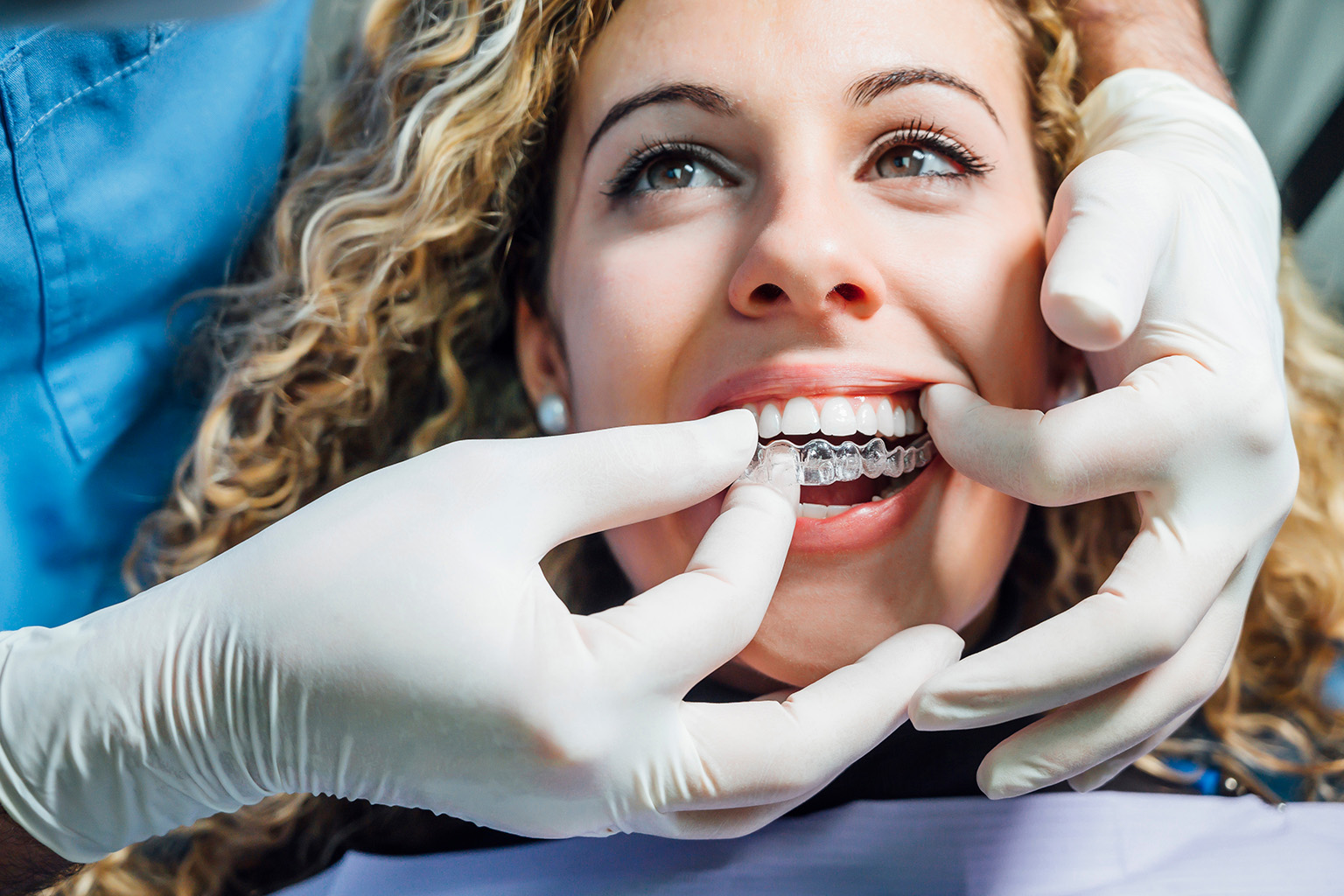 gloved hands placing clear aligner in woman's mouth