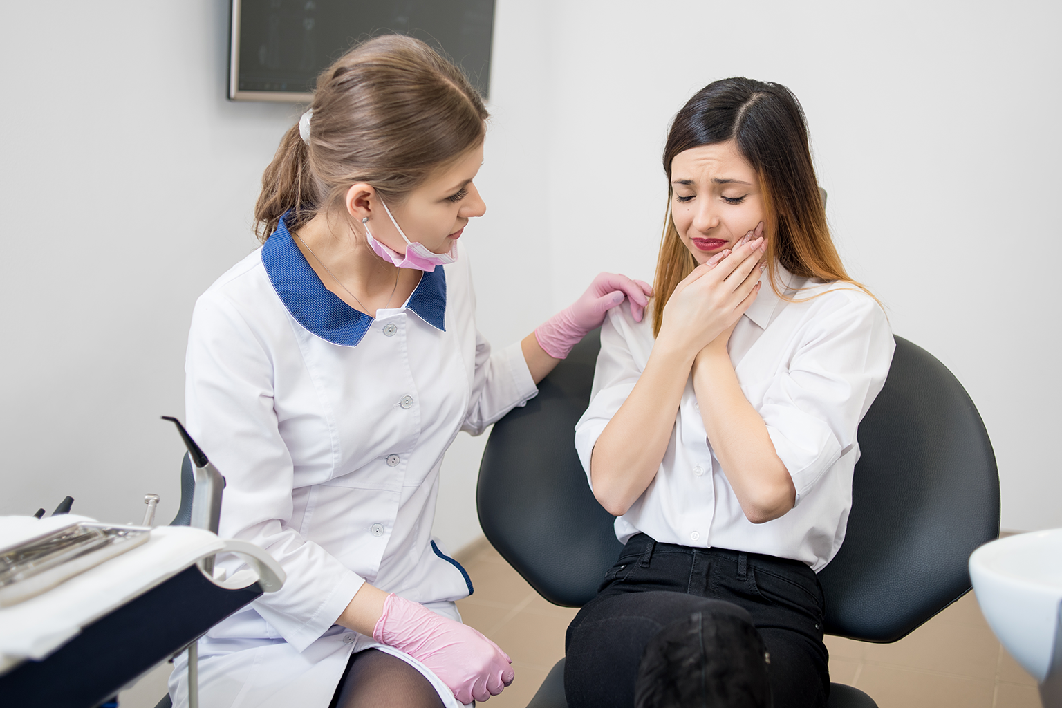 Dentist with hand of shoulder of patient holding her cheek in pain.