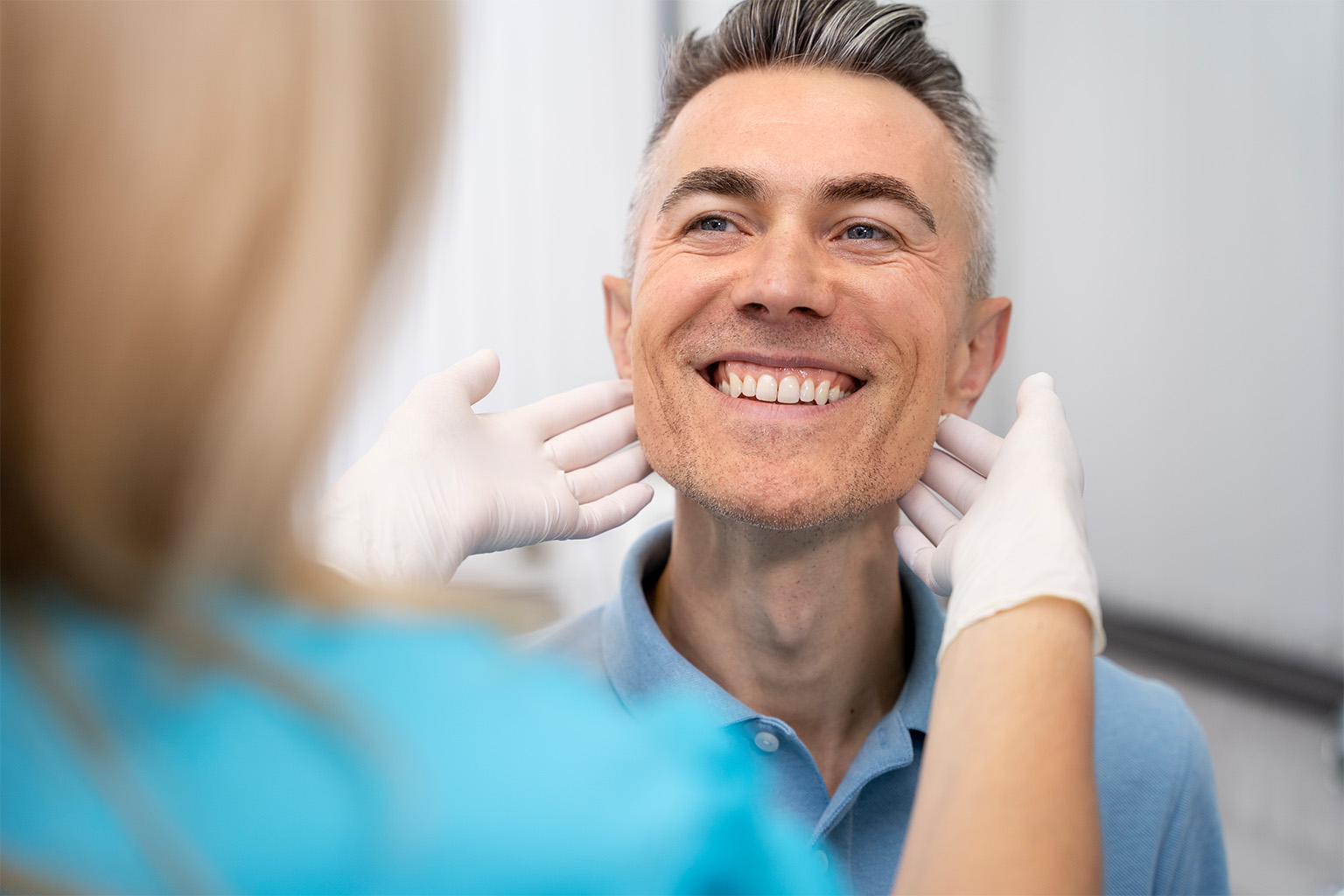 Dentist framing man's face with gloved hands.