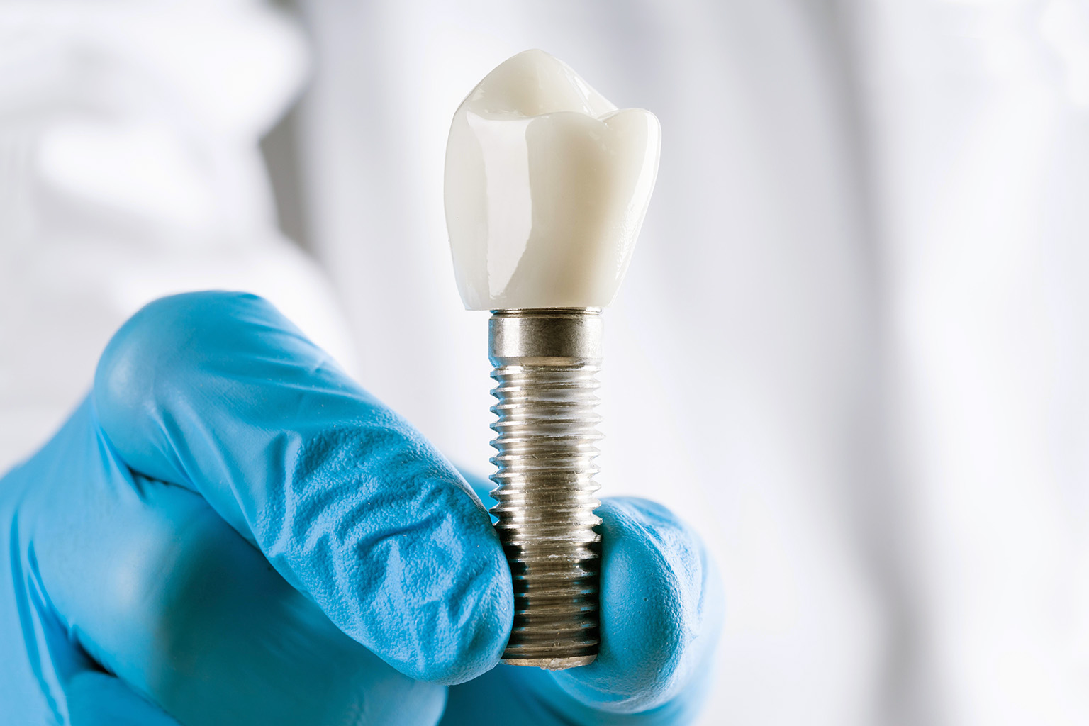 Gloved hand holding large tooth implant model.