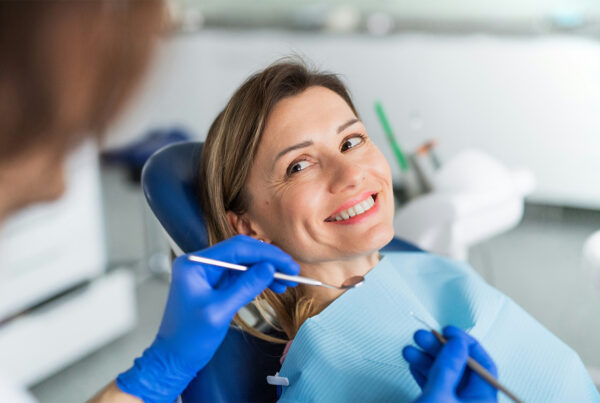 Gloved hands holding dental tools in front of smiling woman.