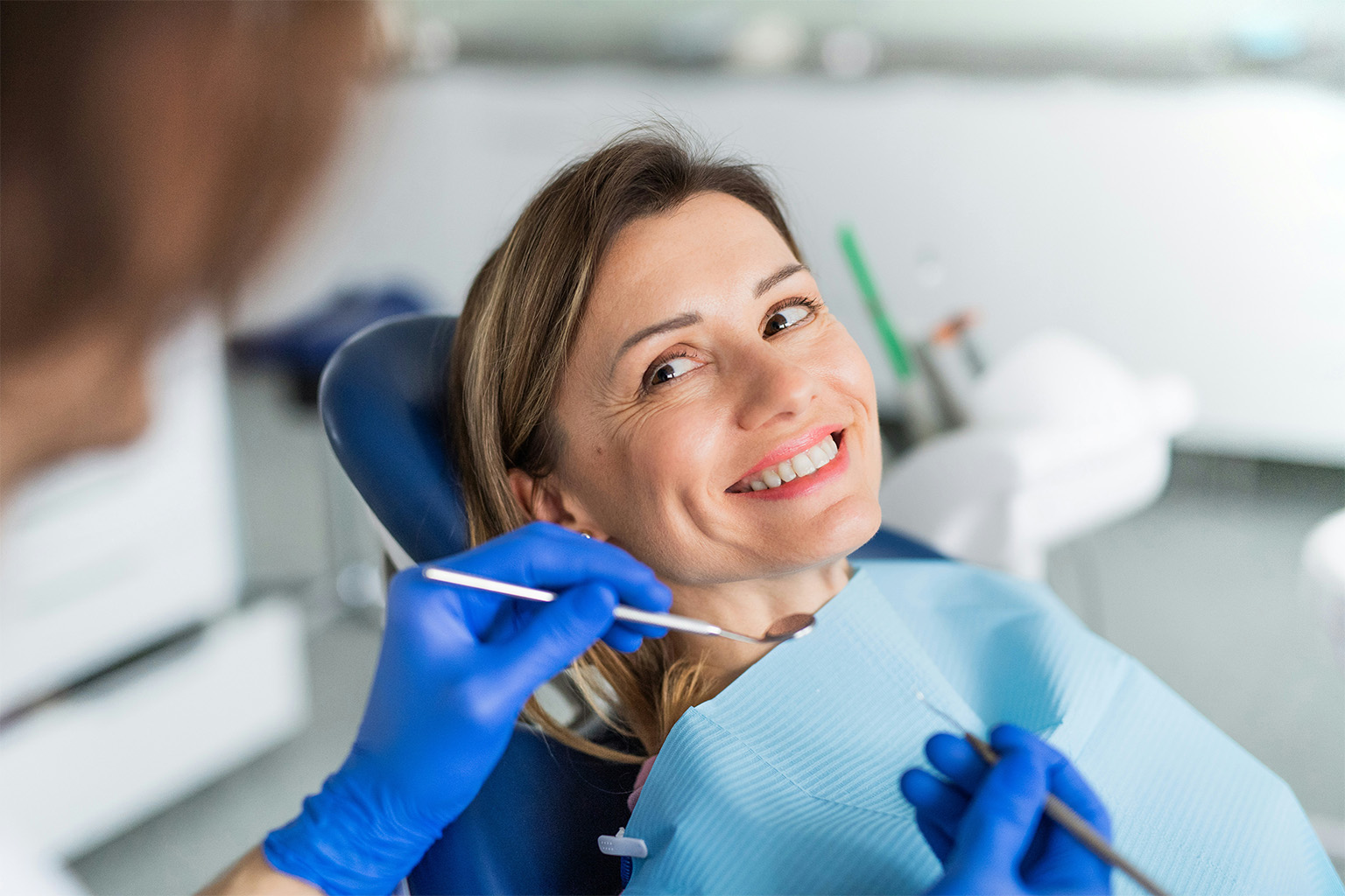 Gloved hands holding dental tools in front of smiling woman.
