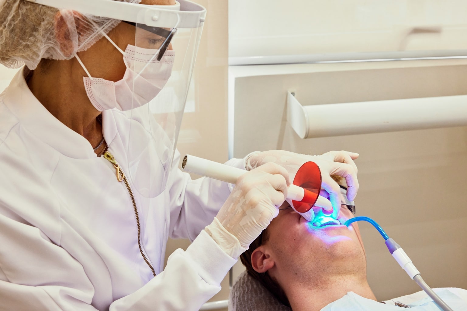 Dentist shining whitening light on patient's teeth.
