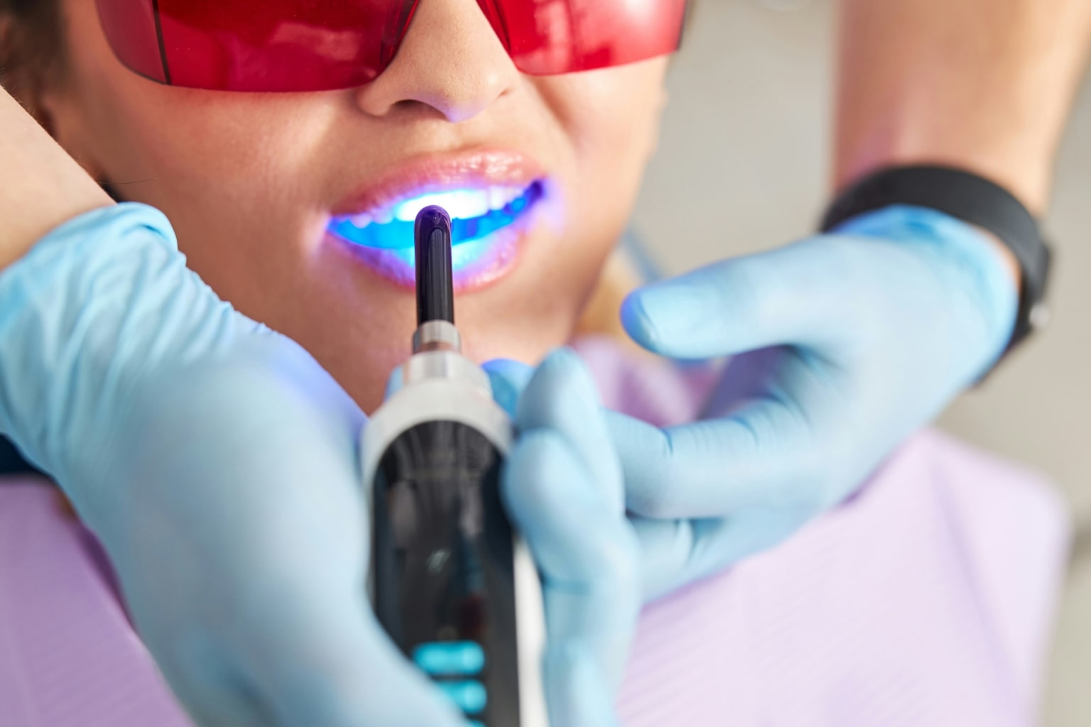 Dentist shining whitening light on patient's teeth.