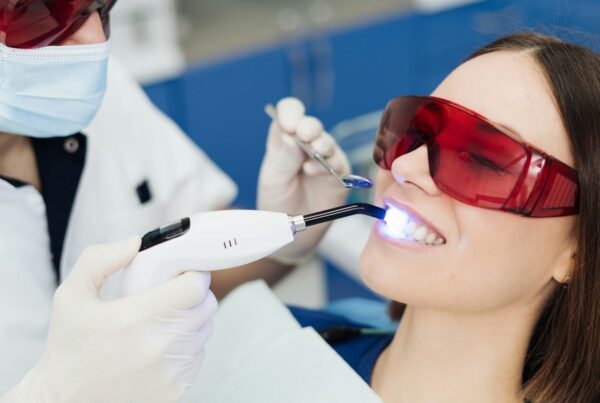 Dentist shining whitening light on patient's teeth.