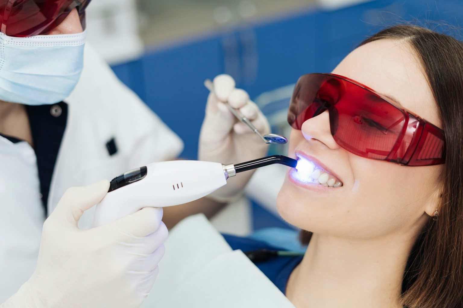 Dentist shining whitening light on patient's teeth.