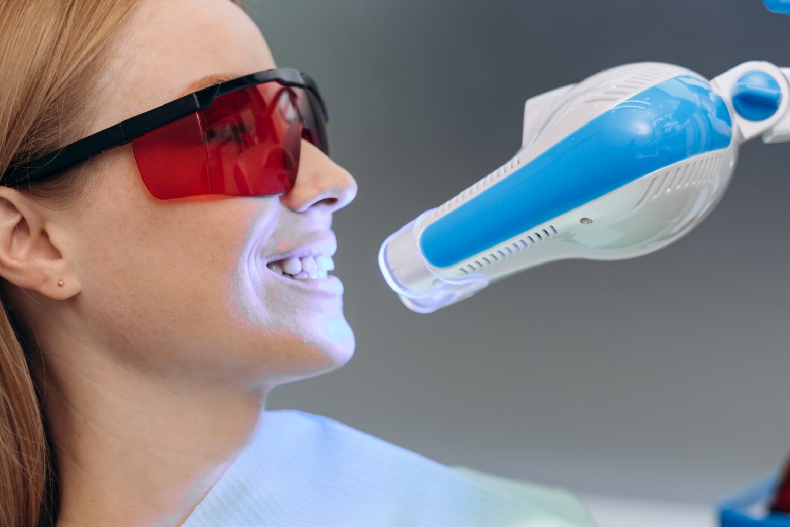Dentist shining whitening light on patient's teeth.