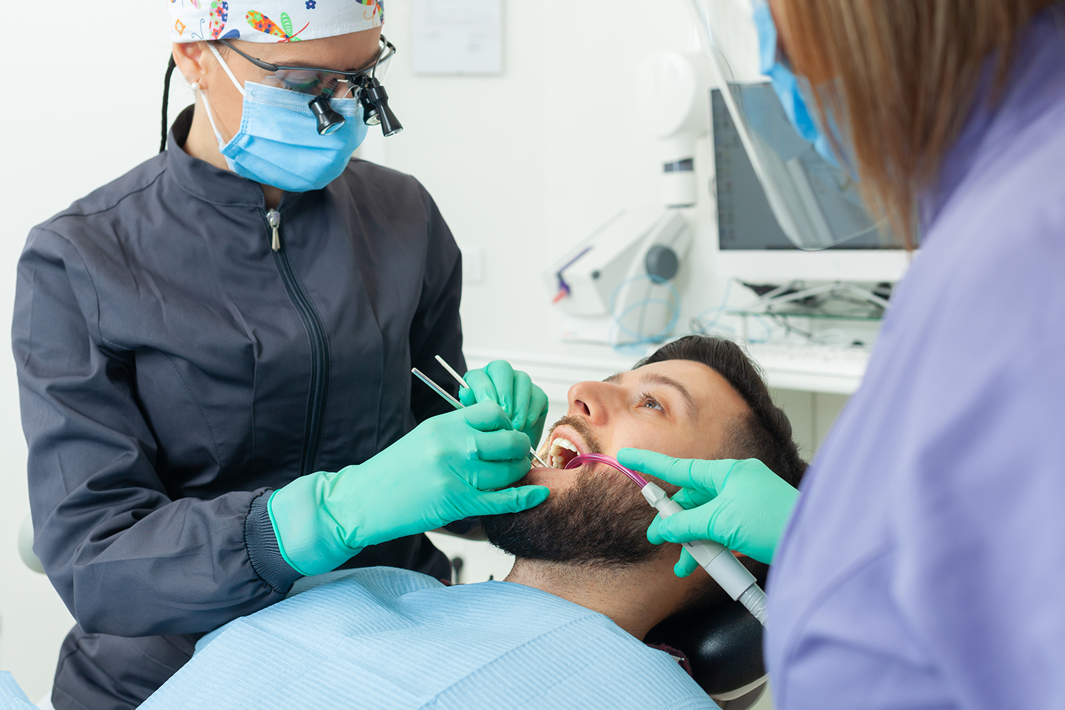 two dentists using dental tools in man's mouth