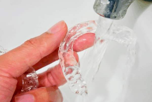Hand holding clear aligner under water faucet.