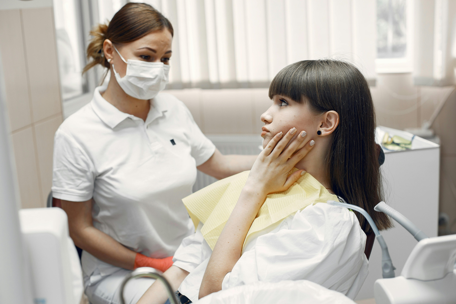 Dentist in mask looking at patient holding her cheek.