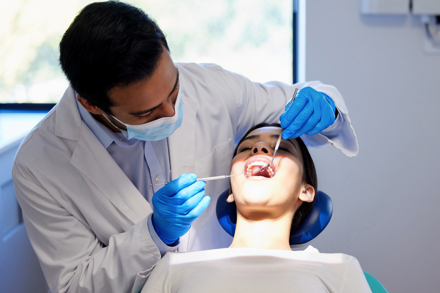 Gloved hands using dental tools in woman's mouth.