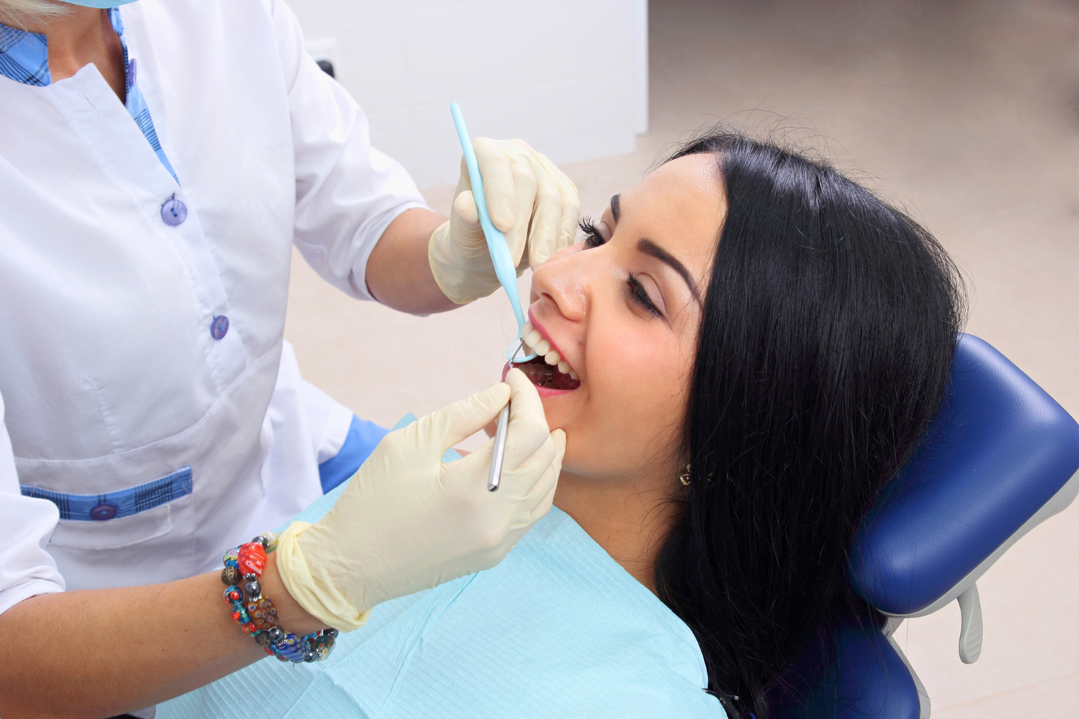 Gloved hands using dental tools in woman's mouth.