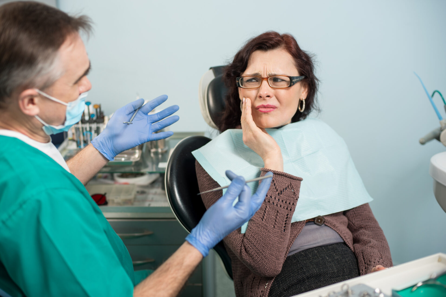 Male dentist talking to female patient holding her cheek.