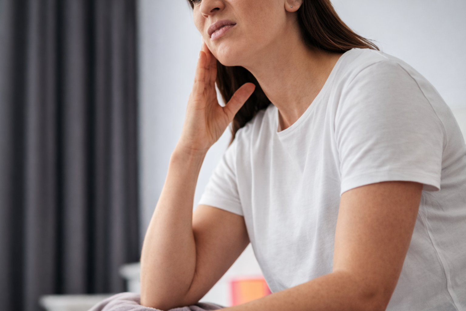 Woman sitting and holding jaw in pain.