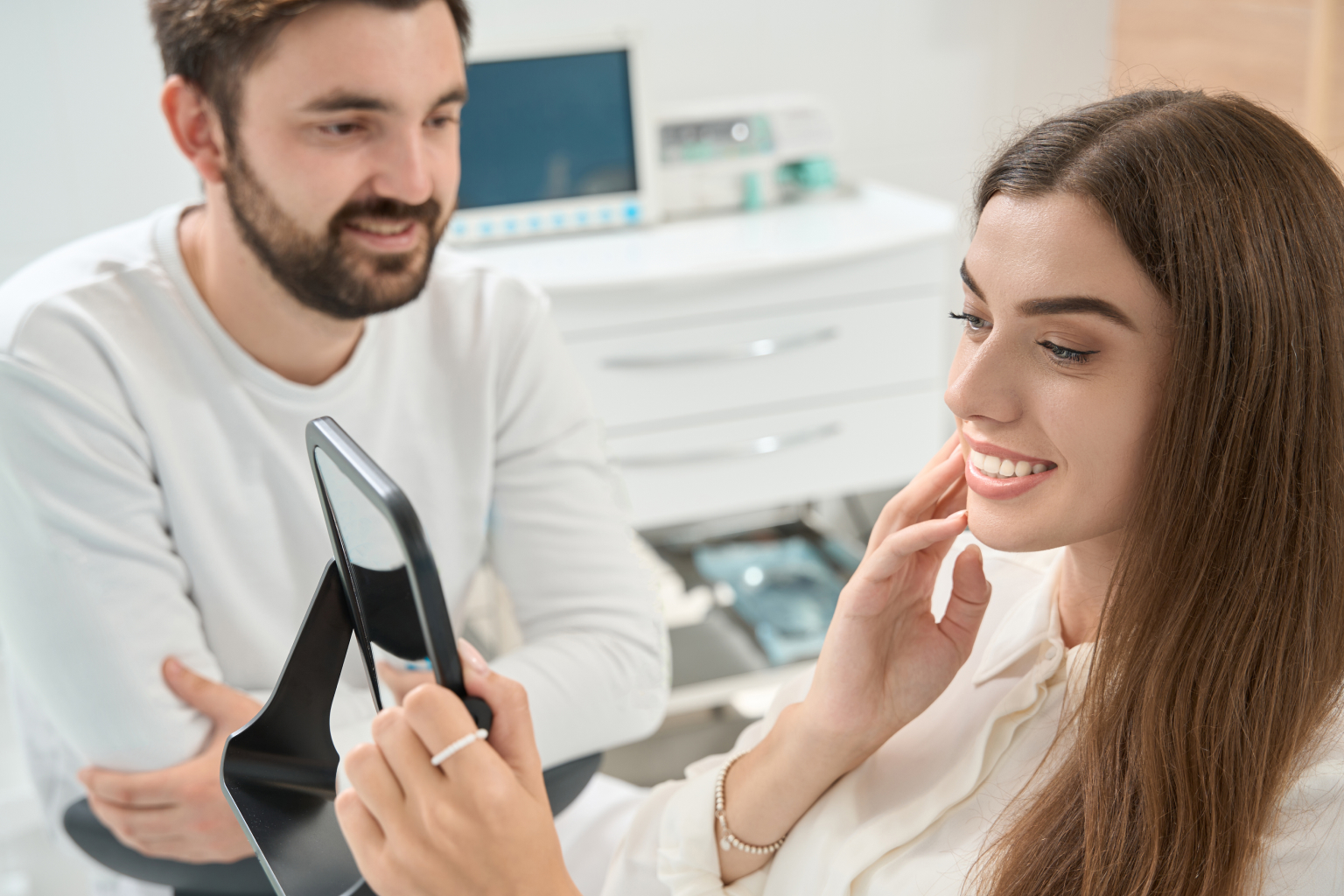 Dentist watching woman look at her smile in hand mirror.